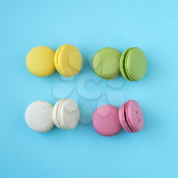Top view of colorful french traditional macarons in yellow, green, white and pink on blue background