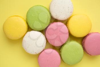 Top view of pink, yellow, white and green traditional french macaroons on  yellow background