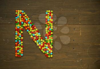Letter N from alphabet made with star shape candy on a wooden background