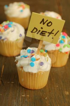 Vanilla cupcake with candies on top and no diet sign on it on a wooden background