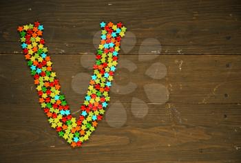 Letter V from alphabet made with star shape candy on a wooden background