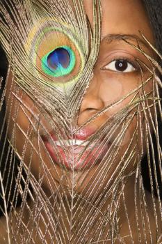 Close-up smiling African-American mid-adult woman looking through peacock feather.