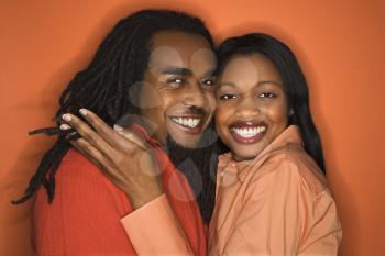 Smiling African-American mid-adult couple wearing orange clothing on orange background.