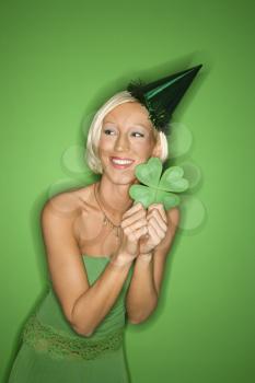 Royalty Free Photo of a Smiling Woman on Green Background Wearing a Party Hat and Holding a Shamrock for Saint Patrick's Day celebration.
