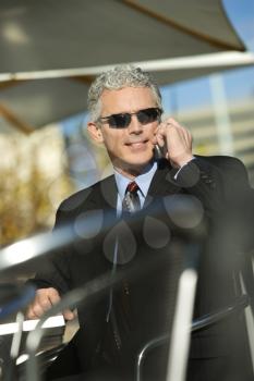 Royalty Free Photo of a Businessman Sitting at a Patio Table Outside Talking on a Cellphone and Smiling