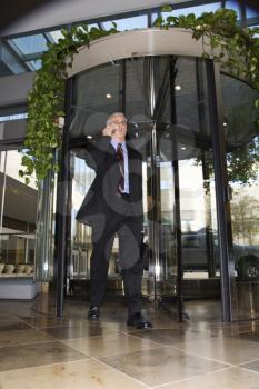 Royalty Free Photo of a Man in a Suit Walking Through a Revolving Door Talking on a Cellphone