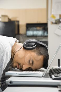 Royalty Free Photo of a Young Man Sleeping With His Head on His Laptop Keyboard While Wearing Headphones