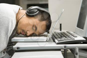 Royalty Free Photo of a Man Sleeping With His Head on a Laptop Keyboard While Wearing Headphones