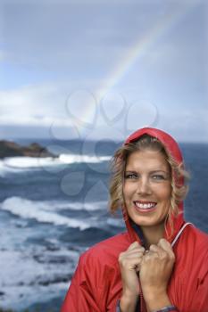 Royalty Free Photo of a Woman in a Red Raincoat in Front of an Ocean With a Rainbow and Smiling in Maui, Hawaii