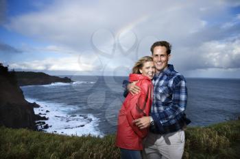 Caucasian mid-adult  couple embracing in front ocean with rainbow in background in Maui, Hawaii.