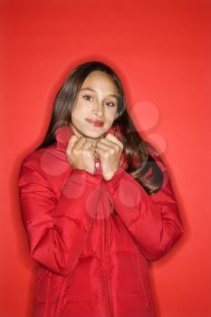Royalty Free Photo of a Teen Girl Holding the Collar of Her Coat and Smiling Standing Against a Red Background