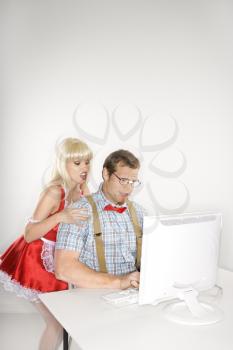 Royalty Free Photo of a Woman Dressed in a French Maid Outfit Whispering to a Man Sitting at a Computer Dressed Like a Nerd
