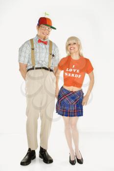 Caucasian young man dressed like nerd wearing propeller hat with Caucasian blonde young woman wearing tshirt reading I love nerds and plaid skirt.