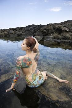 Royalty Free Photo of a Back View of a Sexy Topless Tattooed Woman in a Bikini Sitting in a Tidal Pool in Maui, Hawaii, USA