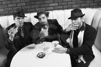 Royalty Free Photo of Three Males in Retro Suits Sitting at a Table With Cocktails