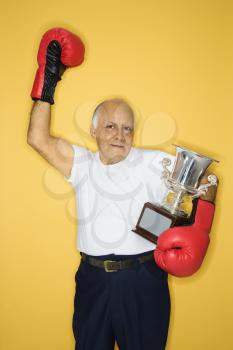 Royalty Free Photo of an Old Man Holding a Trophy and Wearing Boxing Gloves