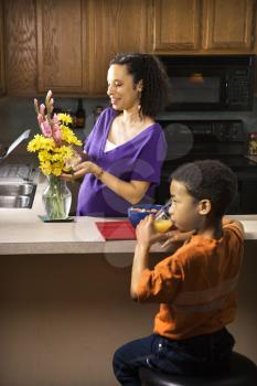 Royalty Free Photo of a Young Pregnant Mother Arranging Flowers While Her Son Eats Breakfast