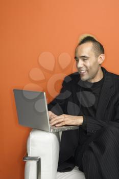 Royalty Free Photo of a Man in Suit with a Mohawk Smiling Typing on Laptop