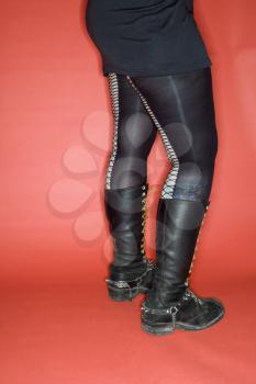 Portrait of woman's lower body weating leggings and boots against orange background.
