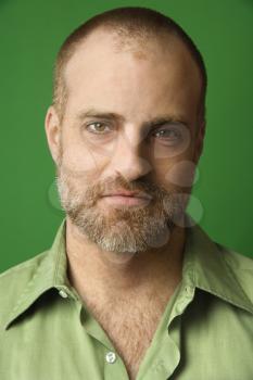 Head and shoulder portrait of Caucasian man with receding hairline and beard against green background.