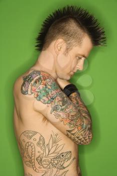 Royalty Free Photo of a Profile of Man with a Mohawk and Tattoos Standing Against a Green Background