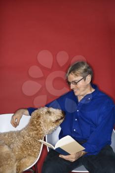 Royalty Free Photo of a Man Sitting With a Golden Doodle Dog and Reading a Book