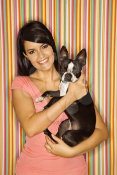 Young adult female Caucasian holding Boston Terrier dog on striped background.