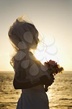 Royalty Free Photo of a Young Bride at Sunset Holding a Bouquet on a Beach