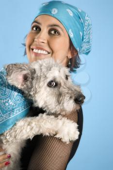 Hispanic mid-adult woman holding small white dog wearing matching bandanas.