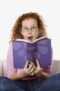 Royalty Free Photo of a Little Girl Sitting and Reading Book Looking Surprised