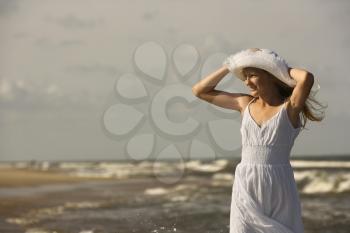 Royalty Free Photo of a Preteen Girl Standing on a Beach Holding Her Hat on Head