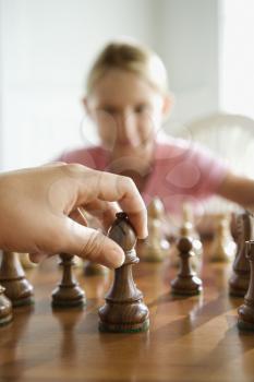 Royalty Free Photo of a Hand Moving a Chess Piece With a Preteen Girl Watching in the Background