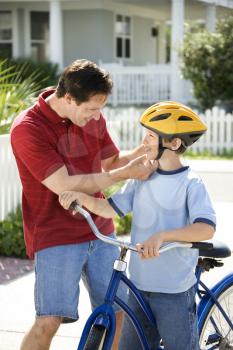 Royalty Free Photo of a Dad Strapping a Bicycle Helmet on His Son