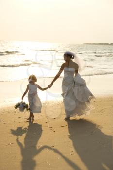 Royalty Free Photo of a Bride and Flower Girl Holding Hands Walking Barefoot on a Beach