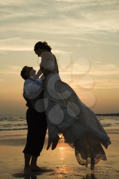 Royalty Free Photo of a Groom Lifting Up a Bride on a Beach at Sunset