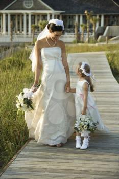 Royalty Free Photo of a Bride Holding Hands With a Flower Girl Walking Down a Wooden Beach Walkway