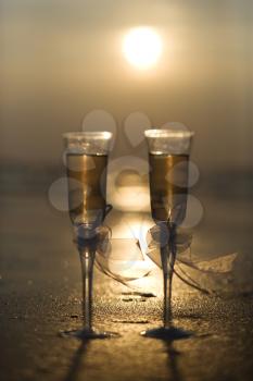 Royalty Free Photo of a Pair of Flute Glasses Filled With Champagne on a Beach at Sunset