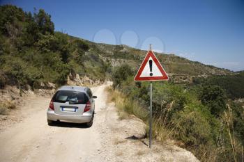 Royalty Free Photo of a Car Heading Down a Dirt Road With a Caution Sign