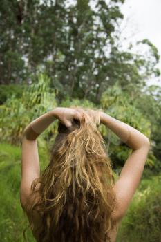 Royalty Free Photo of a Woman in a Lush Forest Holding Up Her Hair