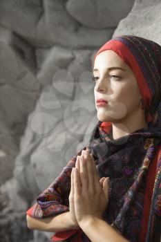 Royalty Free Photo of a Woman Wearing a Scarf Over Her Head Holding Hands to Chest in Prayer Position