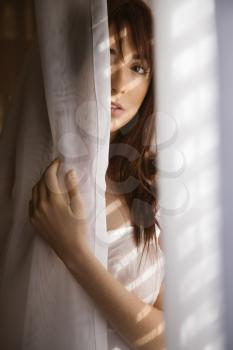 Royalty Free Photo of a Pretty Young Woman Standing in Sunlit Curtains