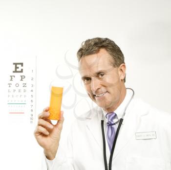 Royalty Free Photo of a Male Doctor Holding a Medical Pill Bottle With an Eye Chart in the Background