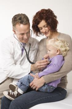Royalty Free Photo of a Male Doctor Holding a Stethoscope to a Toddler's Chest With Her Mother Watching