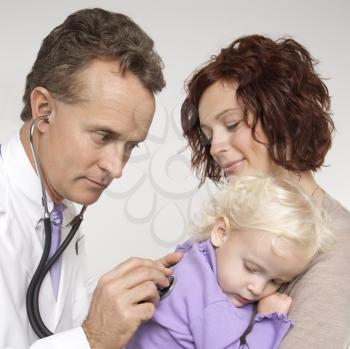 Royalty Free Photo of a Doctor Holding a Stethoscope to a Toddler's Back With a Mother Watching