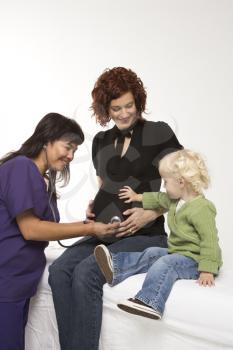 Royalty Free Photo of a Nurse Holding a Stethoscope on a Pregnant Woman's Belly as a Daughter Holds Hand on Her Belly as Well