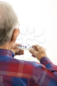 Royalty Free Photo of an Elderly Man Holding Seven-Day Pill Box With Thursday Open
