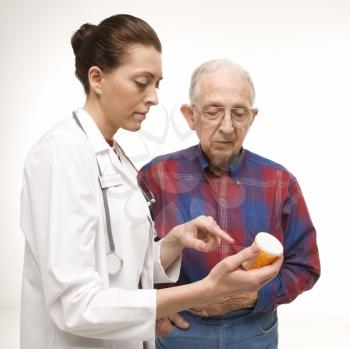 Royalty Free Photo of a Doctor Pointing at a Prescription Bottle as an Elderly Male Looks at the Bottle