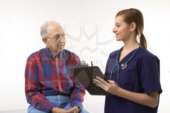 Royalty Free Photo of a Woman in Scrubs Taking Notes From an Elderly Man