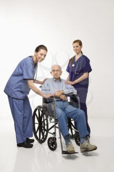 Royalty Free Photo of Two Females Wearing Scrubs With an Elderly Man in a Wheelchair