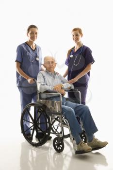 Royalty Free Photo of Two Females Wearing Scrubs With an Elderly Man in a Wheelchair